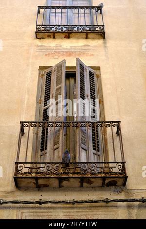 Vista ad angolo basso di una vecchia facciata di casa cittadina mediterranea con alte finestre, persiane di legno e balconi in ferro battuto. Foto Stock