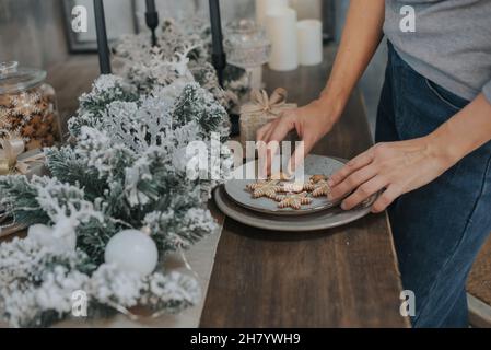 Le mani femminili sono disposte pani di zenzero di Natale a forma di fiocchi di neve su un piatto. Messa a fuoco selettiva. Foto Stock