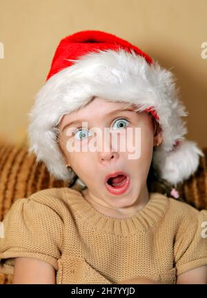 Sorprende la bambina nel cappello di Babbo Natale a casa Foto Stock