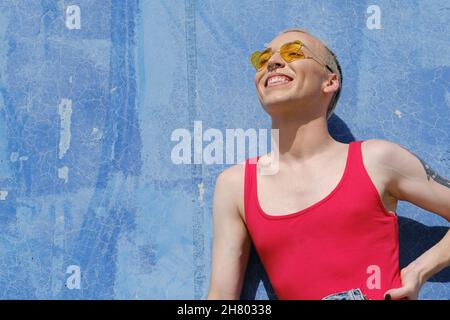 Giovane persona non binaria che indossa occhiali da sole e sorride mentre si posa all'aperto. Foto Stock