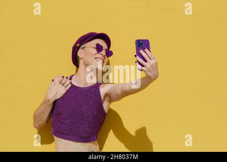 Sorridente persona non binaria divertirsi mentre si prende un selfie con un telefono cellulare all'aperto. Foto Stock