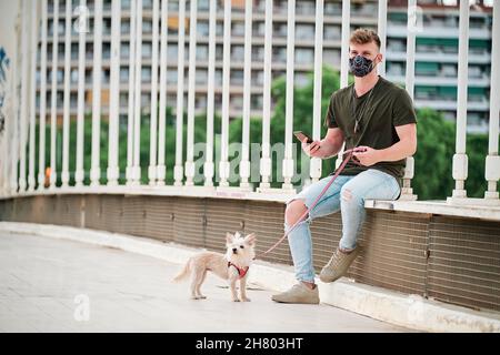 giovane bell'uomo che usa la maschera facciale durante l'epidemia di coronavirus e il suo cane Foto Stock