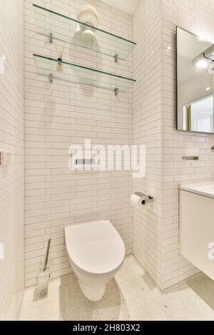 wc in ceramica montato a parete sotto ripiani in vetro in bagno luminoso con specchio riflettente in appartamento Foto Stock
