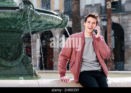 Giovane uomo sorridente mentre parla al telefono all'aperto. Foto Stock