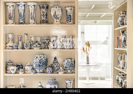 Collezione di vari vasi in ceramica con ornamento bianco e blu posti su mensole in camera luminosa con fiori sul tavolo Foto Stock