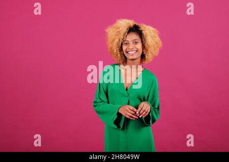 Afro donna in abito verde sorridente mentre in piedi su uno sfondo isolato. Foto Stock