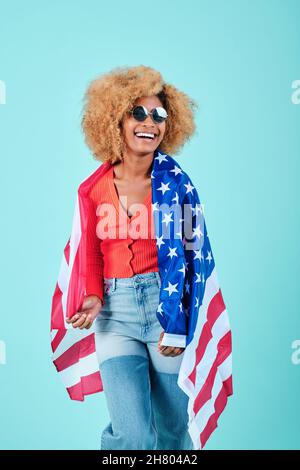 Afro donna in casual vestito sorridendo mentre tiene una bandiera americana su uno sfondo isolato. Foto Stock