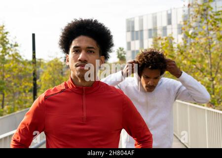 Maschio nero che cammina vicino alla recinzione sulla strada di fronte afroamericano uomo mettere su cuffie Foto Stock