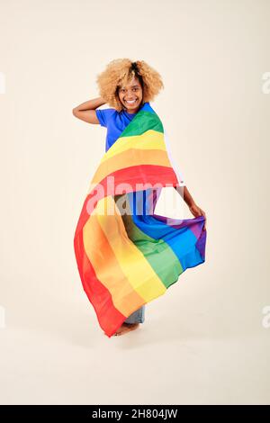 Sorridente capelli ricci donna tenendo una bandiera lgbt orgoglio arcobaleno su uno sfondo isolato. Foto Stock