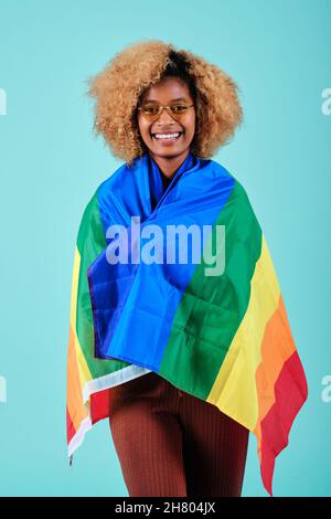 Felice capelli ricci donna sorridente mentre tiene una bandiera arcobaleno del movimento LGBT. Foto Stock