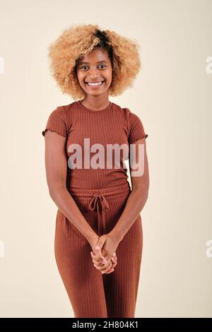 Afro donna che guarda nella fotocamera e sorride mentre si alza su uno sfondo isolato. Foto Stock