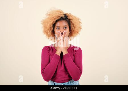 Afro donna che guarda sorpreso la macchina fotografica mentre copre la sua bocca con le mani. Foto Stock