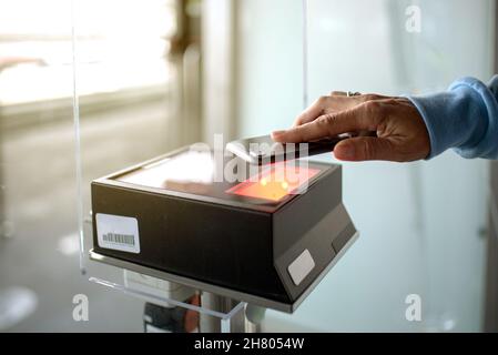 Mano di persona senza volto raccolto con carta d'imbarco digitale per scansione smartphone mentre si trova nel moderno terminal dell'aeroporto prima della partenza Foto Stock