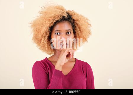 Afro donna mettere il dito in bocca mentre si fa un gesto di silenzio su uno sfondo isolato. Foto Stock