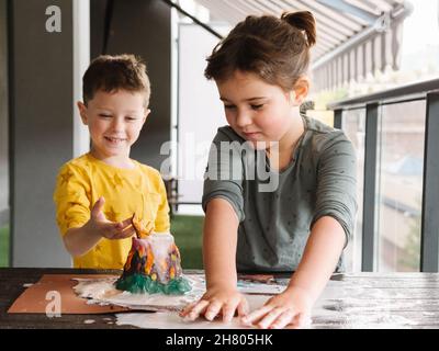 Adorabile bambina rotolare plastilina, mentre la creazione di figurine vulcaniche fatte a mano con fratello felice in asilo Foto Stock