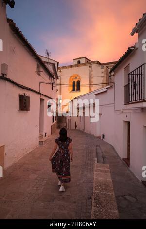 Indietro view femmina turista passeggiando su strada lastricata tra case antiche sulla strada di Setenil de las Bodegas in serata Foto Stock