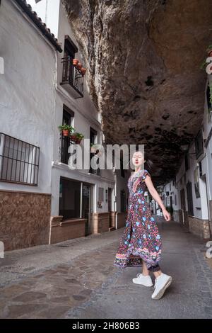 Pieno corpo di allegro viaggiatore asiatico femminile in abito guardando la macchina fotografica mentre si trova in piedi su strada lastricata vicino vecchie case Foto Stock