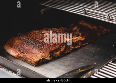 Deliziose costolette di maiale alla griglia con crosta posta su una griglia in metallo in una moderna macchina per barbecue con rack in un bar leggero Foto Stock