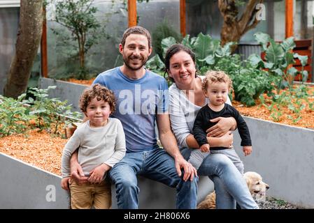 Genitori felici con figli carini seduti sul letto del giardino con cucciolo Golden Retriever in campagna guardando la macchina fotografica Foto Stock