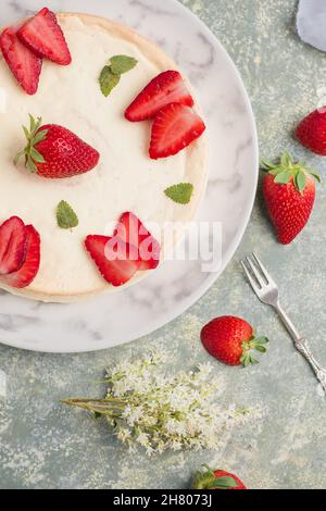Gustosa cheesecake rotonda decorata con fragole mature e foglie di menta verde servite su piatto al tavolo in cucina leggera Foto Stock