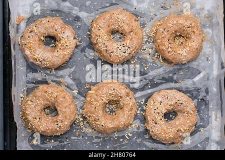 Vista dall'alto di bagel a basso contenuto di carboidrati non cotti cosparsi di semi di sesamo posti su carta da forno su vassoio in cucina leggera Foto Stock