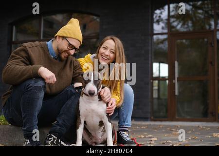 Coppia di contenuti guardando la macchina fotografica seduta su scale con Bull Terrier vicino casa porta di vetro in autunno Foto Stock