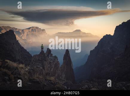 Scenario mozzafiato di anonimo viaggiatore maschile in piedi su ruvida scogliera rocciosa e osservare il paesaggio incredibile contro cielo nuvoloso tramonto durante le escursioni Foto Stock