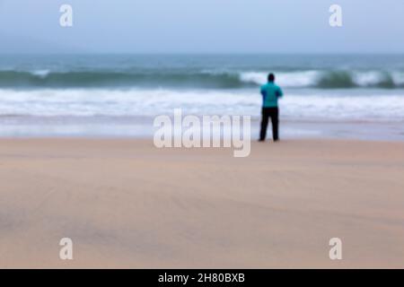 Vista posteriore dell'uomo in piedi sulla riva del mare a Luskenthire Beach, Isola di Lewis e Harris, Ebridi esterne, Scozia Regno Unito nel mese di novembre - belle arti sfocate Foto Stock