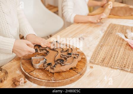 le mani dei bambini carve i biscotti sulla pasta di pan di zenzero dalle figurine. Ragazza che prepara i biscotti di natale su un tavolo di legno Foto Stock