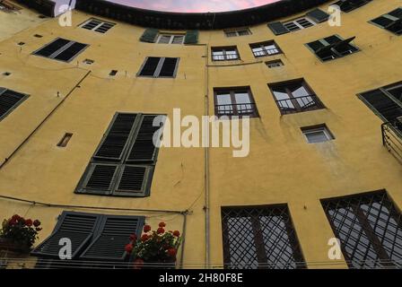 La forma ellittica dell'anfiteatro romano di Lucca, Toscana, Italia, è conservata nelle concave pareti esterne di queste case medievali che circondano Piazza dell'Anfiteatro, spazio pubblico aperto creato nel 1830 sul sito dell'antica arena. Le loro pareti posteriori convesse sono costruite in mattoni e macerie di pietra che riempiono enormi archi romani che un tempo sostenevano la cavea, le file di posti a sedere che potrebbero ospitare fino a 10,000 spettatori. Foto Stock