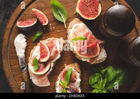 Bruschetta con prosciutto e formaggio italiano e fichi su un asse di legno, vista dall'alto Foto Stock