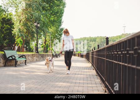 Donna caucasica in una maschera medica sul suo viso a piedi il suo cane labrador Retriever in quarantena. Pandemia di coronavirus. Foto Stock