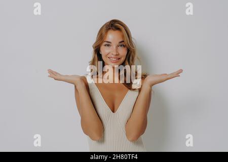 Positivo leggermente confuso con bel sorriso biondo giovane donna solleva le mani in esitazione Foto Stock