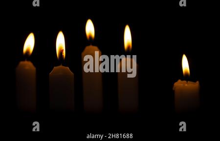 Cinque candele di Natale su sfondo scuro. Candele che bruciano al buio. Foto Stock
