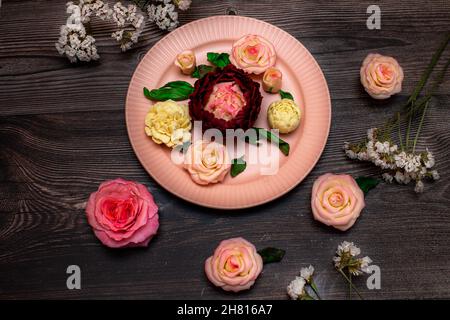 Rose rosa al cioccolato, rose bianche, peonie sono nel piatto rosa su uno sfondo di legno scuro. Foto Stock