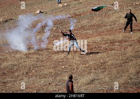 Nablus, Cisgiordano, Palestina. 26 novembre 2021. Il dimostratore palestinese lancia barattoli di gas lacrimogeni ai soldati israeliani durante una dimostrazione contro gli insediamenti israeliani nel villaggio di Beit Dajan vicino alla città di Nablus in Cisgiordania. Credit: Nasser Ishtayeh/ZUMA Wire/Alamy Live News Foto Stock