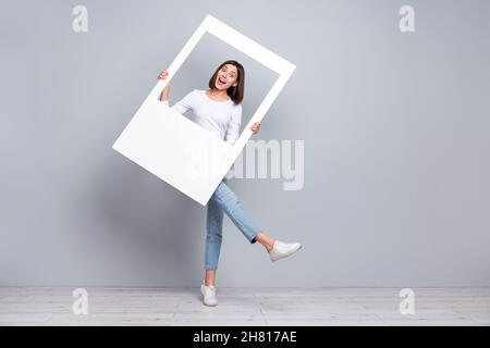 Foto del corpo intero di bruna impressionata giovane donna telaio indossare camicia jeans sneakers isolato su sfondo grigio Foto Stock