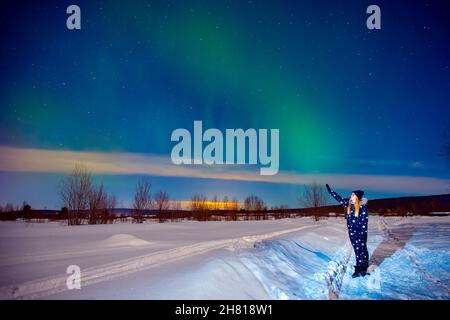 Donna turistica guarda aurora notte aurora luci nord a foresta, fuoco morbido. Foto Stock