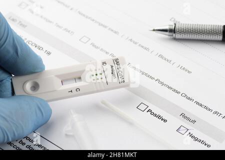 Primo piano del dispositivo di test rapido dell'antigene che mostra un risultato negativo del test per SARS-COV-2, COVID-19, tenuto in mano su carta per documenti di test. COVID-19, testina Foto Stock