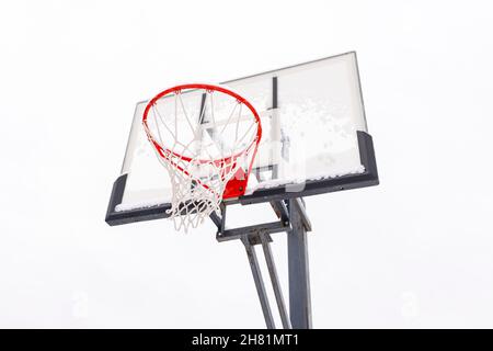 Cerchio di basket rosso su una tavola posteriore su uno sfondo chiaro, vista dal basso. Attrezzature sportive per una partita di palla all'aperto di squadra. Telaio in acciaio, protezione in plexiglass. Foto Stock