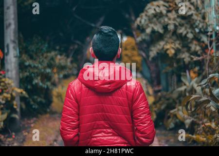 Giovane maschio che indossa un cappotto rosso che cammina in un parco Foto Stock