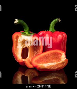 Peperoni dolci, rossi, interi e tagliati a pezzi, su sfondo nero con riflessi Foto Stock