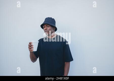 Giovane uomo nero in abiti Street-style che tiene la sua bevanda da asporto su uno sfondo bianco Foto Stock