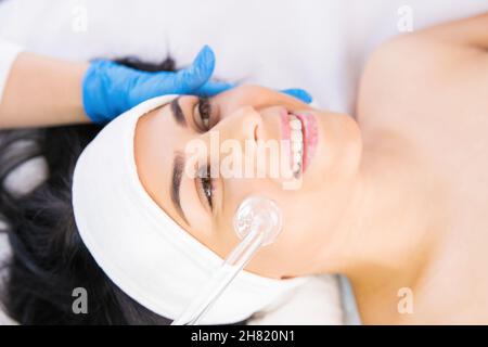 Il cosmetologo fa la procedura per il peeling della pelle del viso di una bella donna in un salone di bellezza, cosmetologia e cura professionale della pelle. Foto Stock