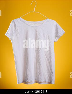 t-shirt in cotone bianco ricalcato appesa a un appendiabiti su sfondo giallo, abiti estivi Foto Stock