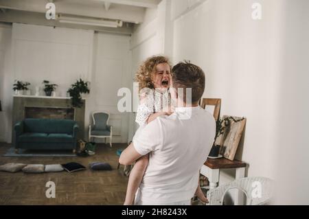 una bambina con capelli ricci piange tra le braccia del papà, tristezza dei bambini Foto Stock