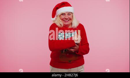 Anziano anziano bella nonna donna indossa rosso maglione di Capodanno e cappello sorridente guardando la macchina fotografica Foto Stock