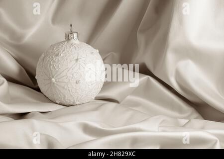Decorazione bauble natalizia bianca su seta avorio con spazio per la copia del testo. Carta di Natale o disegno di invito della festa. Foto Stock