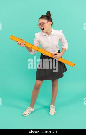 Una ragazza in età scolare è seduta ad un tavolo e si concentra sul taglio  di gioielli e regali di carta con forbici di cancelleria. Capelli lunghi e  testa Foto stock 