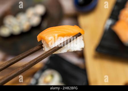 Tenere un nigiri salmone norvegese con bacchette di legno da portare in bocca Foto Stock